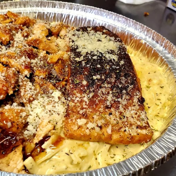 Grilled salmon and chicken with parmesan cheese over pasta in a foil takeout container.