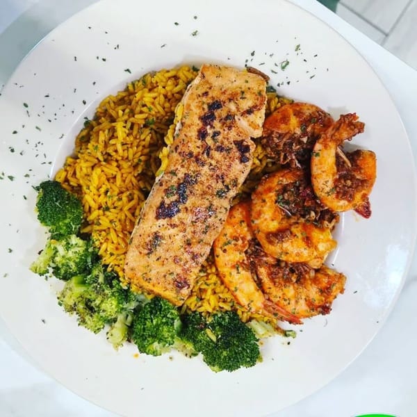 Grilled salmon and shrimp with yellow rice and broccoli on a white plate.