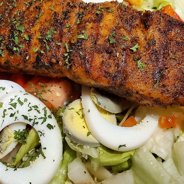 Close-up of a seasoned salmon fillet on a bed of fresh salad with sliced eggs and tomatoes.