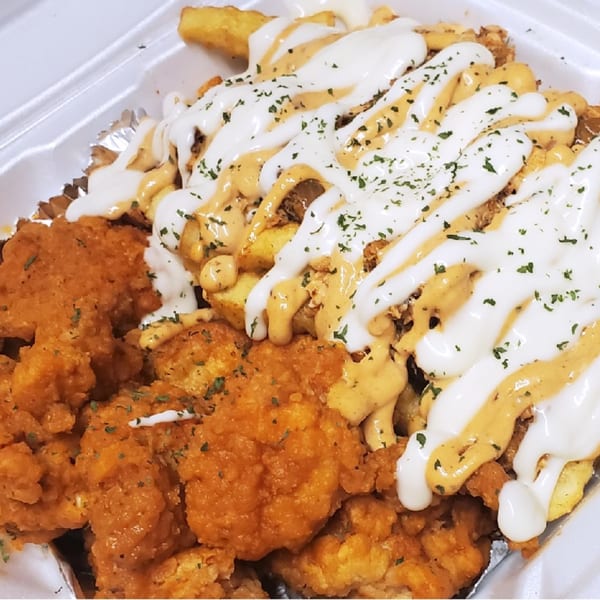 Crispy fried chicken and french fries drizzled with white and orange sauces, garnished with parsley.
