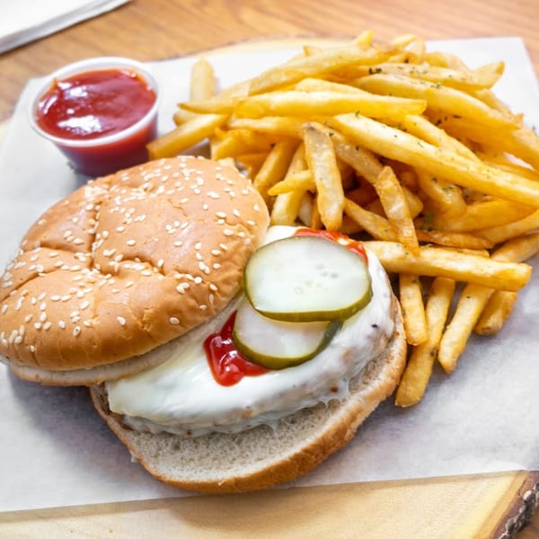 A burger with pickles, ketchup, and mayonnaise, served with a side of french fries and ketchup.
