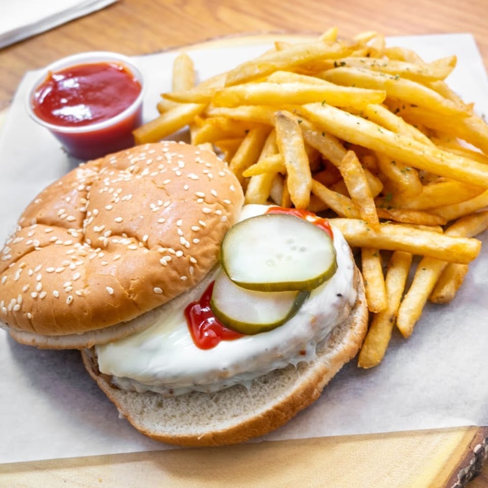 A burger with pickles, ketchup, and mayonnaise, served with a side of french fries and ketchup.