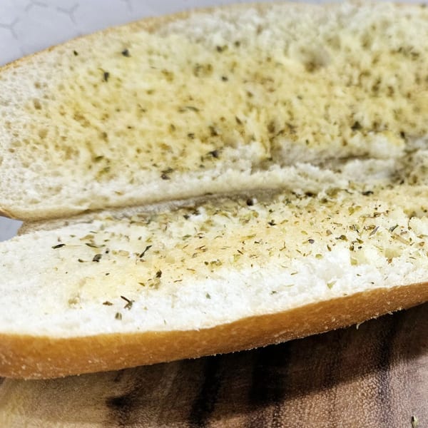 Two halves of garlic bread, seasoned with herbs, ready to be served at Lagos Island Pizza & Grille.
