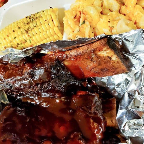 BBQ ribs in foil with corn on the cob and macaroni and cheese in a takeout container.