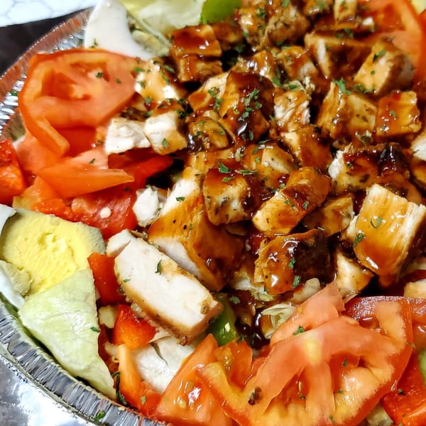 A close-up of a Lagos Island Pizza & Grille salad with chicken, tomatoes, and lettuce.